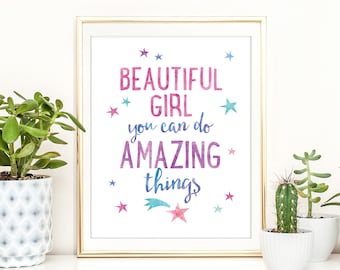 以下が含まれることがあります： 「BEAUTIFUL GIRL you can do AMAZING things」という言葉がピンクと青の水彩文字で書かれた、額縁に入ったプリント。さまざまな色の星の形で装飾されています。フレームは金色です。