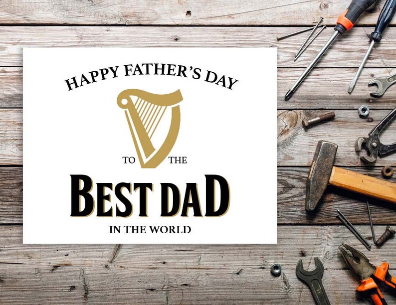 May include: White card with black text that reads "Happy Father's Day to the Best Dad in the World". A gold harp logo is above the text. The card is on a wooden surface with tools and nails.