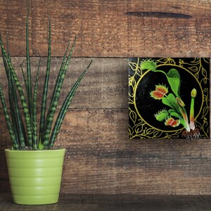 Peut inclure: Une peinture d'une plante carnivore avec des feuilles vertes et des fleurs rouges sur un fond noir avec des accents dorés. La peinture est encadrée dans un cadre doré.