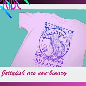 May include: A pink t-shirt with a blue and purple graphic of a jellyfish. The graphic is surrounded by a decorative frame and the text "Jellyfish" is below the graphic. The text "Jellyfish are non-binary" is below the image.