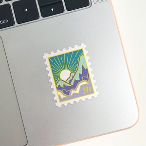 May include: A vintage-style postage stamp sticker with a blue, green, and yellow mountain landscape design. The stamp has a yellow border and says "19&cent;" in the bottom right corner.