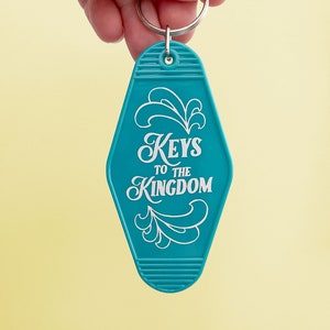 K&ouml;nnte beinhalten: Ein t&uuml;rkisfarbener Motel-Schl&uuml;sselanh&auml;nger mit dem Text "Keys to the Kingdom" in wei&szlig;en Buchstaben. Der Schl&uuml;sselanh&auml;nger hat einen silbernen Schl&uuml;sselring.