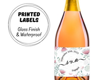 May include: A bottle of sparkling wine with a floral design label. The label says "September 10th, 2022" and "s&a Engaged".