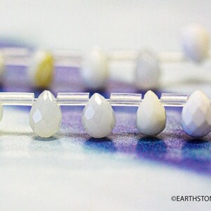 May include: A strand of white teardrop-shaped beads strung on a clear elastic cord. The beads have a faceted, iridescent finish.