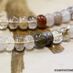 May include: A strand of clear, white, gray, and brown gemstone beads. The beads are round and have a smooth, polished finish.