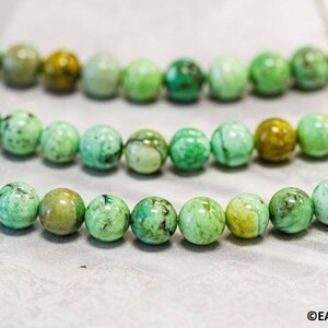 May include: Three strands of round, polished beads in varying shades of green. The beads have a marbled appearance, with some displaying darker green and brown inclusions. The beads are strung together, suggesting they are for jewelry making.