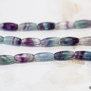 May include: A strand of oval-shaped beads made of green, purple, and white fluorite. The beads are strung on a clear thread.