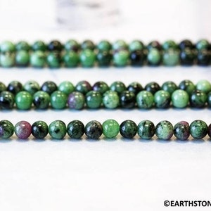 May include: A strand of green and pink gemstone beads. The beads are round and have a smooth, polished finish.