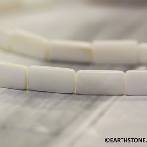 May include: A strand of white rectangular shell beads. The beads are smooth and have a slight iridescent sheen.