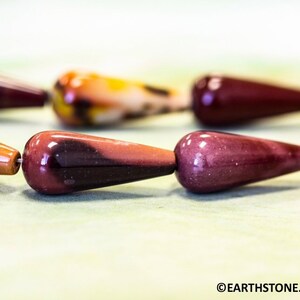 May include: A strand of polished gemstone beads in shades of red, brown, and white. The beads are teardrop shaped and have a glossy finish.