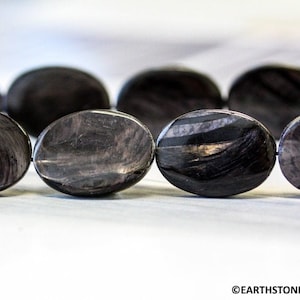 May include: A strand of oval-shaped black and grey gemstone beads. The beads have a striated pattern.