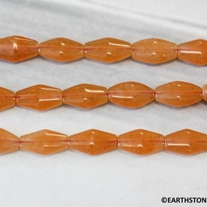 May include: A strand of orange gemstone beads with a faceted, oval shape. The beads are strung on a clear thread and are arranged in three rows.