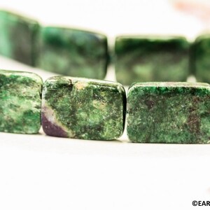 May include: A strand of green and black gemstone beads, each bead is rectangular and has a unique pattern.