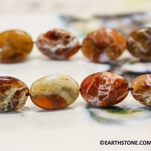 May include: A strand of oval-shaped carnelian beads with brown, orange, and white patterns. The beads are strung on a thin wire.