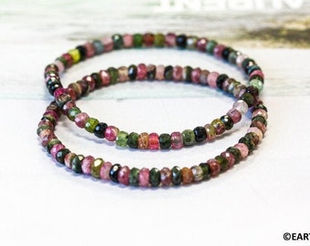 May include: Two bracelets made of small, multi-colored gemstone beads. The beads are pink, green, and black. The bracelets are stacked on top of each other.