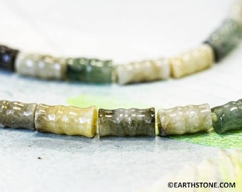 May include: A strand of jade beads, each bead is a different shade of green, brown, and yellow. The beads are shaped like short cylinders and have a smooth, polished finish.