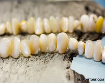 May include: A strand of white and cream colored iridescent shell beads. The beads are oval shaped and have a smooth, polished finish.