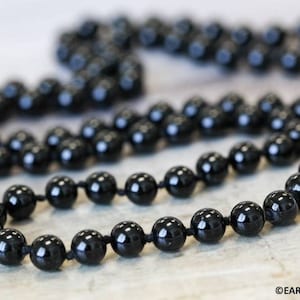 May include: A black onyx beaded necklace with a shiny finish. The beads are strung on a black cord and the necklace is approximately 30 inches long.