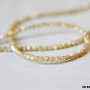 May include: Two strands of delicate, cream-colored beaded bracelets. The beads are small and have a slightly iridescent sheen.