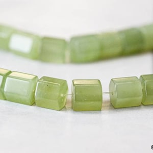 May include: A strand of light green jade beads, each bead is a square with rounded edges. The beads are strung on a clear thread.