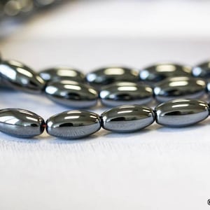 May include: A strand of black hematite beads, each bead is oval shaped and has a smooth, polished finish.