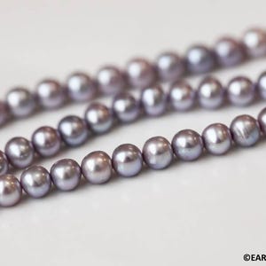 May include: A strand of lavender-colored freshwater pearls. The pearls are round and smooth, and they are strung on a clear thread.