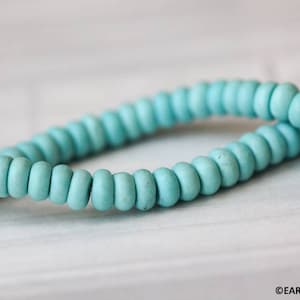 May include: A strand of light blue turquoise beads. The beads are round and smooth, and they are strung together on a clear thread.