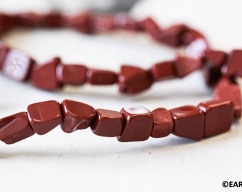 May include: A strand of dark red gemstone beads, each bead is a unique, irregular shape. The beads are strung on a clear thread.
