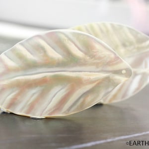 May include: Two iridescent white leaf-shaped pendants with a hole at the top for stringing.