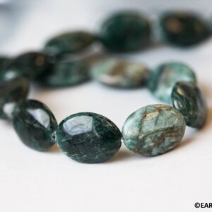 May include: A strand of oval-shaped green and white gemstone beads. The beads are strung together on a clear thread. The beads are smooth and polished.