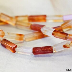 May include: A strand of carnelian beads with a mix of opaque white and translucent orange-red colors. The beads are rectangular and have a polished finish.