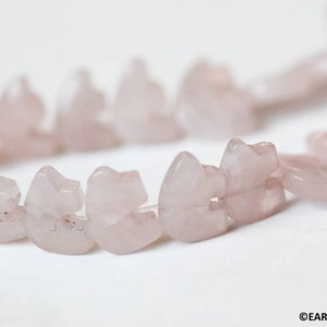May include: A strand of pink rose quartz beads, each carved into a heart shape. The beads are strung together on a clear thread.