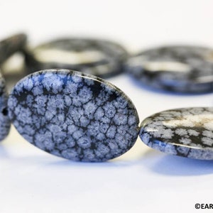 May include: A strand of oval-shaped, gray and white snowflake obsidian beads. The beads have a unique, speckled pattern.
