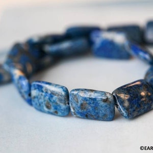 May include: A close-up of a blue lapis lazuli gemstone bracelet. The bracelet is made of rectangular beads with a mottled blue and white pattern.