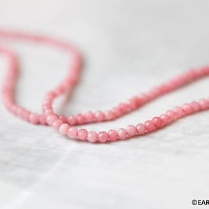 May include: A strand of pink gemstone beads, strung on a thin cord. The beads are small and round, and they have a smooth, polished finish.