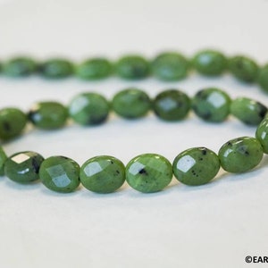 May include: A strand of green jade beads with a faceted oval shape. The beads are strung on a clear thread and have a natural, earthy look.