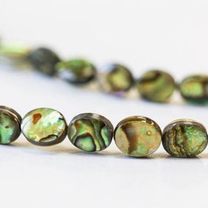May include: A strand of oval-shaped abalone shell beads with iridescent green, brown, and gold colors.