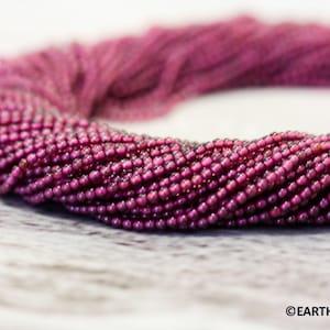 May include: A strand of deep pink gemstone beads. The beads are small and round, and they are strung together in a long, continuous strand.