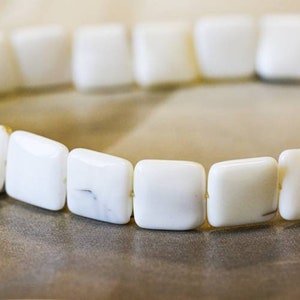 May include: A white square-shaped bead bracelet made of smooth, polished white beads.