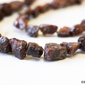 May include: A strand of dark red, rough-cut gemstone beads. The beads are irregular in shape and have a natural, unpolished look.