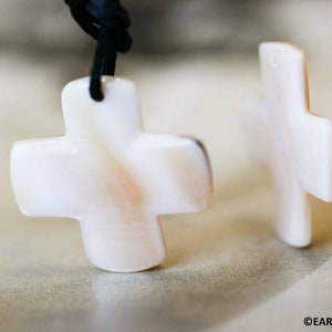 May include: Two white shell cross pendants on black cords. The crosses are smooth and have a natural, slightly iridescent finish.