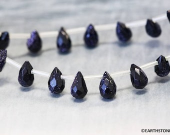 May include: A strand of dark blue gemstone beads in a teardrop shape. The beads are strung on a clear elastic cord.