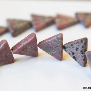 May include: A strand of pink and black triangle-shaped beads made of natural stone. The beads are strung on a wire and are ready to be used for jewelry making.