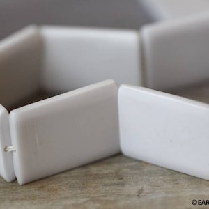 May include: White hexagonal ceramic beads strung together on a white cord. The beads are smooth and glossy.