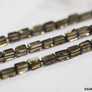 May include: A strand of smoky quartz beads, each bead is faceted and has a square shape. The beads are strung on a clear thread.