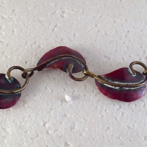 May include: A red and silver bracelet with a leaf design. The bracelet is made of metal and has a hook clasp.