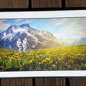 May include: Two white stormtrooper figures riding a tandem bicycle in a field of yellow dandelions with a snow-capped mountain in the background.