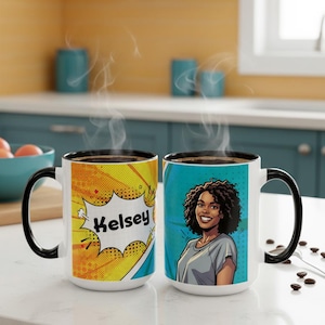 May include: Two white ceramic mugs with black handles and rims. One mug features the name "Kelsey" in a comic book style speech bubble against a yellow and orange background. The other mug has an illustration of a woman with curly hair.