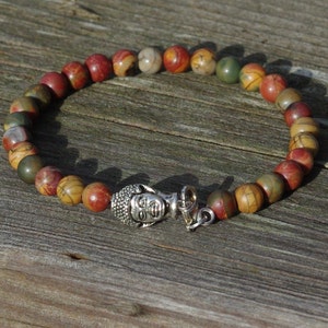 May include: A beaded bracelet with a silver Buddha charm. The beads are multi-colored with shades of red, brown, yellow, and green.