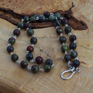 May include: A necklace made of green, red, and black speckled beads with a silver clasp.
